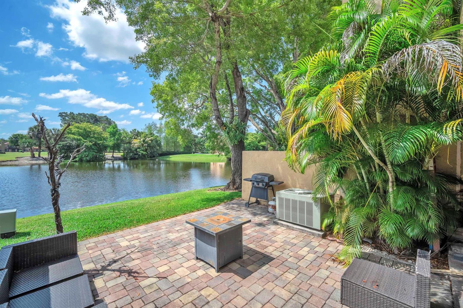 A paved patio overlooks a lake with a grill, fire pit, and lush palm trees — 740 E Coco Plum Circle # 3, Plantation FL 33324, PLANTATION, FL
