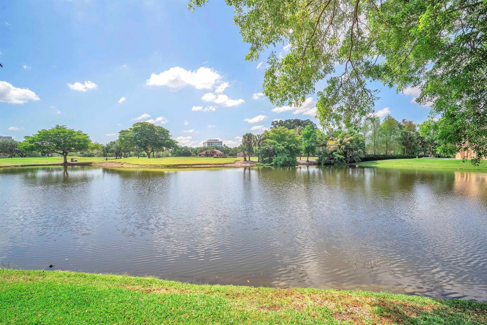 A pond sits in the foreground of a grassy golf course with trees and buildings — 740 E Coco Plum Circle # 3, Plantation FL 33324, PLANTATION, FL