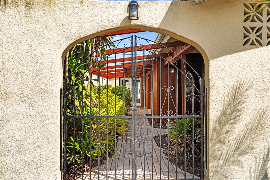 A wrought iron gate opens to a paved walkway leading to a house entrance — 10472 ORANGE BLOSSOM LANE, SEMINOLE, FL
