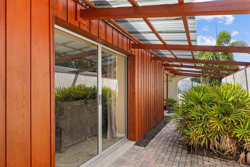 A patio with a wooden pergola, sliding glass doors, and a brick walkway beside plants — 10472 ORANGE BLOSSOM LANE, SEMINOLE, FL