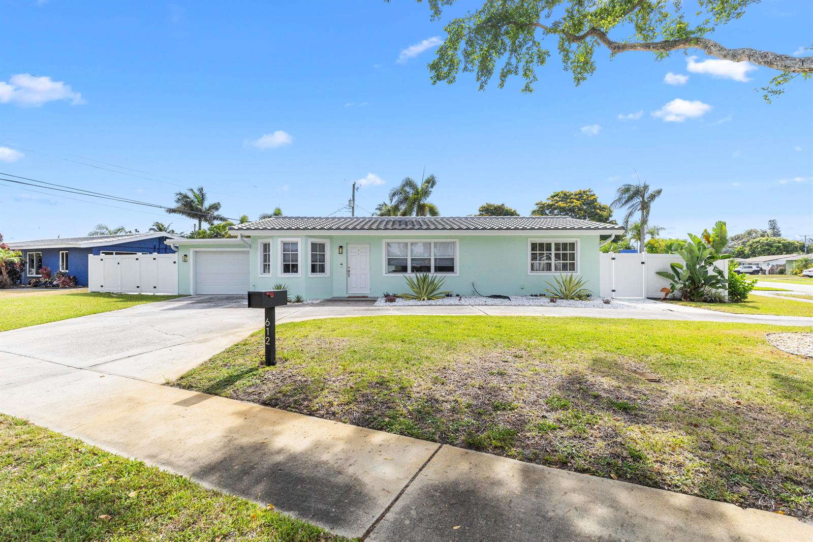 A light green single-story house features a white garage door and a concrete driveway — 612 SE 10th Avenue, Deerfield Beach FL 33441, DEERFIELD BEACH, FL
