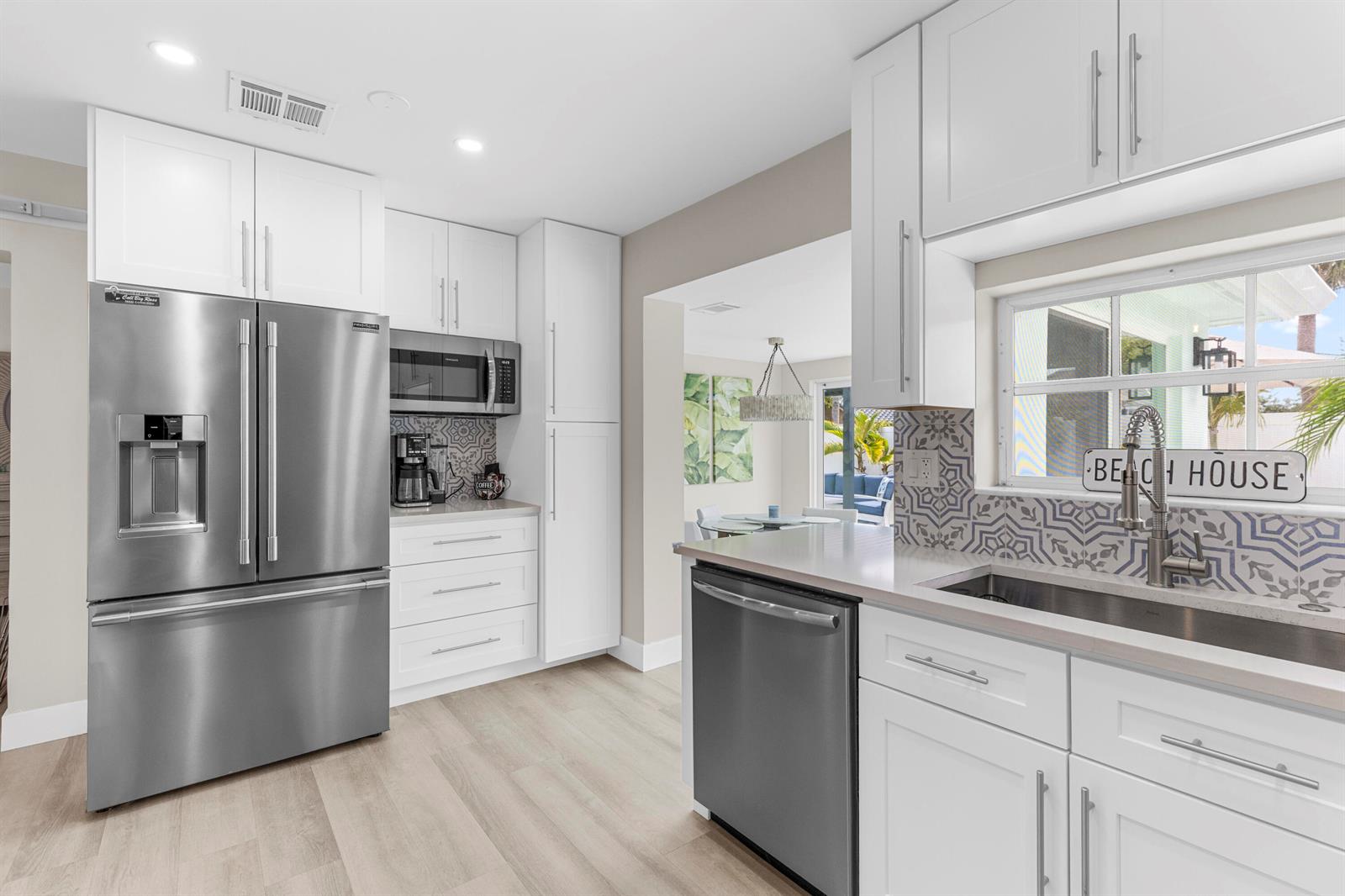 A white kitchen features patterned tile backsplashes, stainless steel appliances, and a peninsula counter — 612 SE 10th Avenue, Deerfield Beach FL 33441, DEERFIELD BEACH, FL