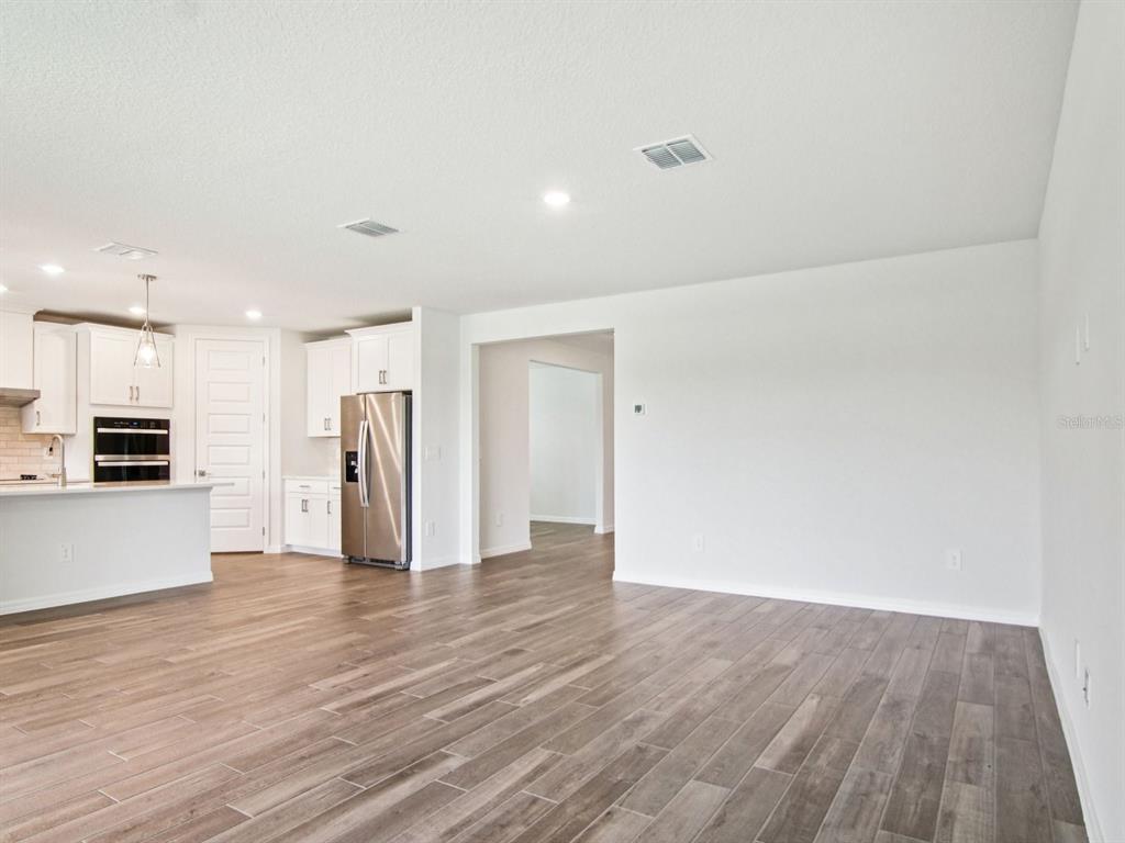 A bright, open-concept kitchen and living area featuring white cabinetry and wood-look tile flooring — 36712 MELSTONE WAY, ZEPHYRHILLS, FL