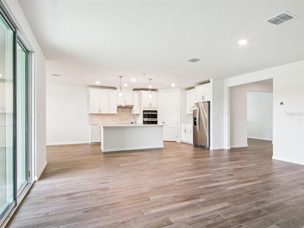 A modern kitchen features white cabinets, a central island, stainless steel appliances, and wood-look flooring — 36712 MELSTONE WAY, ZEPHYRHILLS, FL