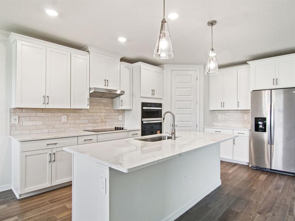 A modern kitchen features white cabinets, a large quartz island, and stainless steel appliances — 36712 MELSTONE WAY, ZEPHYRHILLS, FL