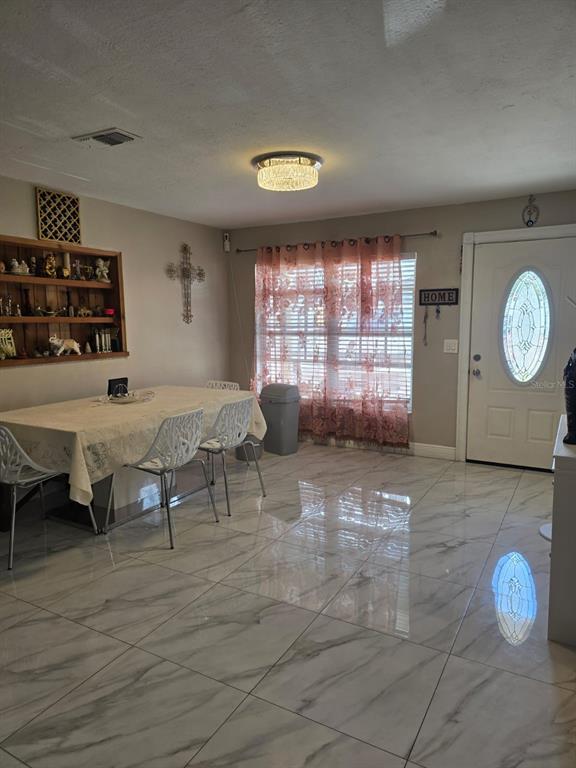 A dining area features a table with white chairs, marble-look tile flooring, and a front door — 10325 LOUBET STREET, ORLANDO, FL