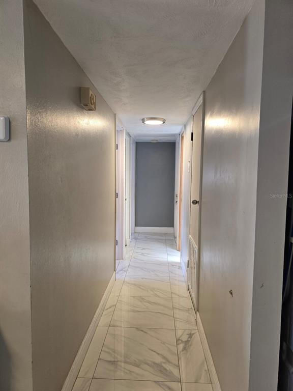 A narrow hallway features white marble-look tile flooring and light gray walls — 10325 LOUBET STREET, ORLANDO, FL