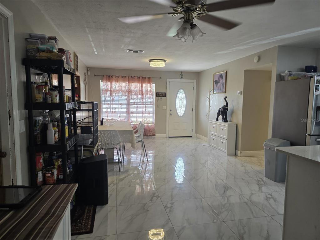 A dining area with white marble-look tile flooring, a ceiling fan, and a front door — 10325 LOUBET STREET, ORLANDO, FL