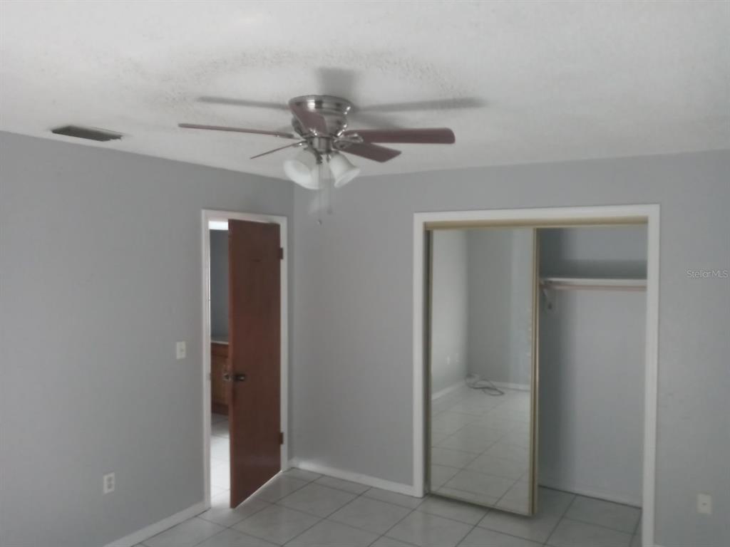 A bedroom with gray walls, tile flooring, a ceiling fan, and a mirrored closet door — 26645 COUNTY ROAD 561 UNIT 3, TAVARES, FL