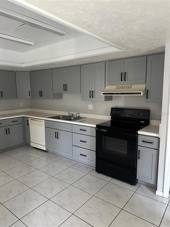 A kitchen features gray cabinets, white countertops, a black stove, and light-colored tiled flooring — 26645 COUNTY ROAD 561 UNIT 3, TAVARES, FL