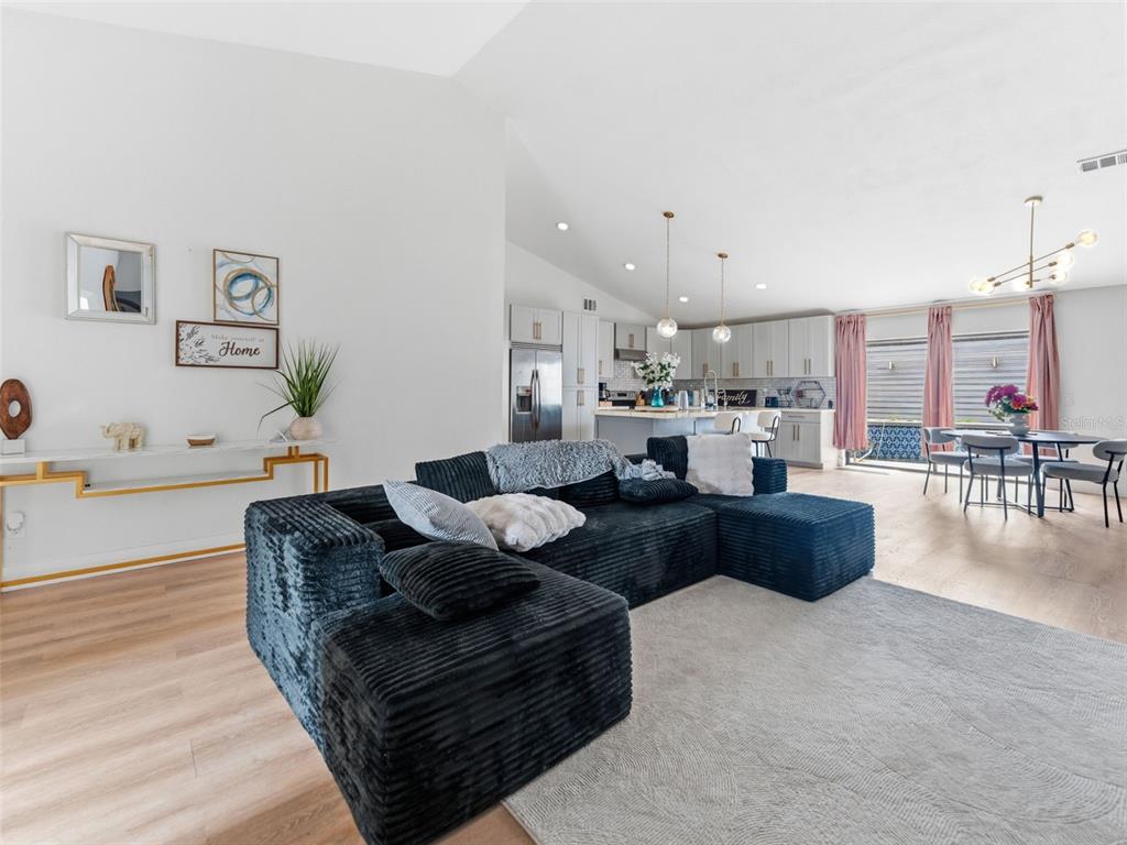 A living room with a large black sectional sofa, light wood floors, and an open kitchen — 530 RAPID FALLS DRIVE, BRANDON, FL