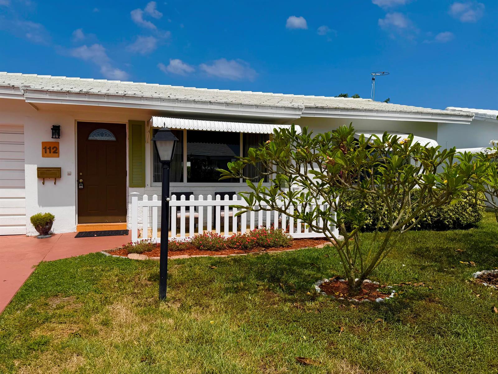 A single-story house exterior features a brown front door, white picket fence, and front lawn — 112 SW 9th Street, Boynton Beach FL 33426, BOYNTON BEACH, FL