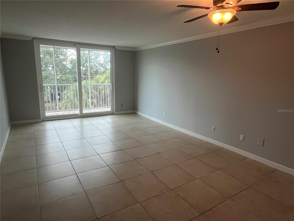 An empty living room features light-colored tile flooring, gray walls, and a sliding glass door — 2650 COCONUT BAY LN LANE UNIT 532, SARASOTA, FL