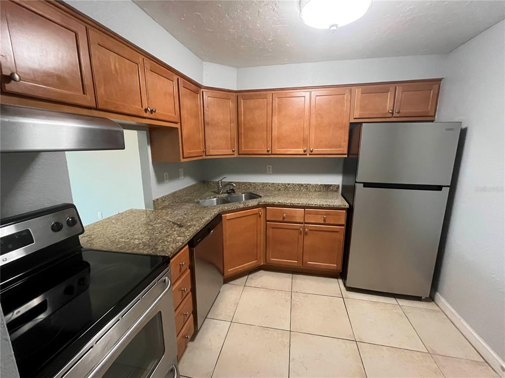 A kitchen features wood cabinets, granite countertops, stainless steel appliances, and light-colored tile flooring — 2650 COCONUT BAY LN LANE UNIT 532, SARASOTA, FL
