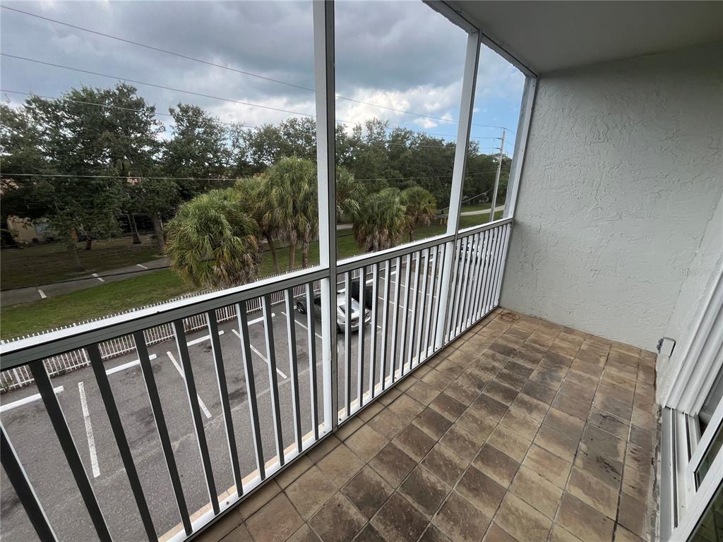 A screened-in balcony with tiled flooring overlooks a parking lot and trees — 2650 COCONUT BAY LN LANE UNIT 532, SARASOTA, FL