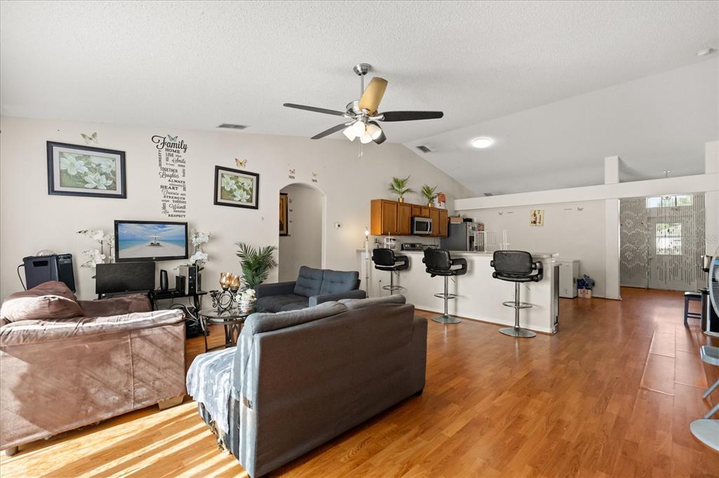 A living room with wood flooring, a ceiling fan, and an open kitchen with bar seating — 1321 DUNBARTON COURT, KISSIMMEE, FL