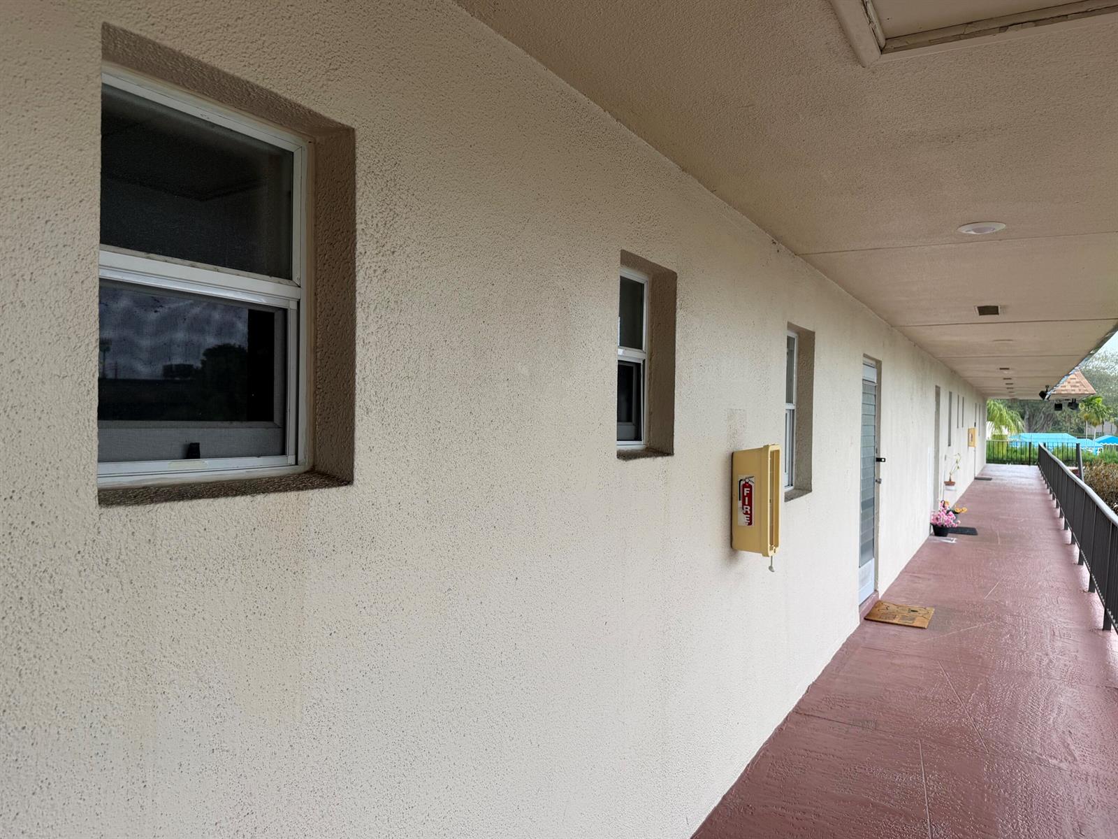 An exterior walkway with a fire extinguisher cabinet, windows, and doors along a stucco wall — 502 Davis Road # 6, Palm Springs FL 33461, PALM SPRINGS, FL