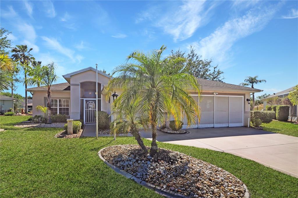 A single-story house with a palm tree, a rock garden, and a screened garage door — 20631 PRINCE RANIER PLACE, LEESBURG, FL