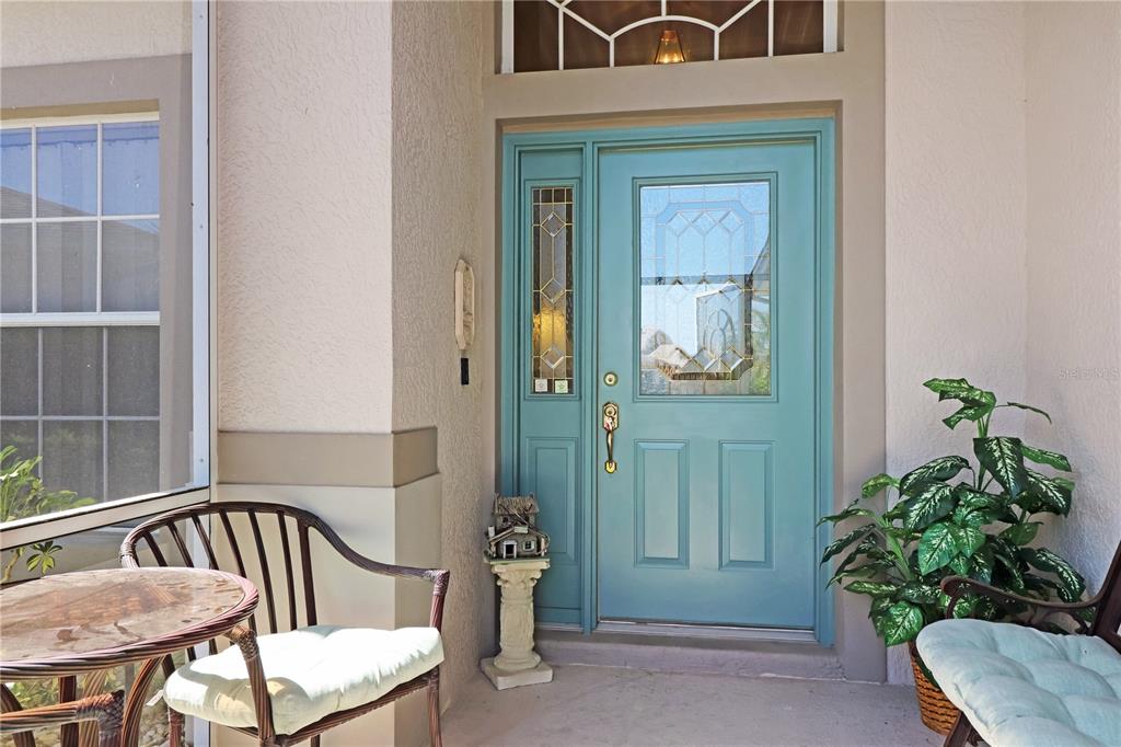 A teal front door with a glass insert and sidelight sits on a covered porch — 20631 PRINCE RANIER PLACE, LEESBURG, FL