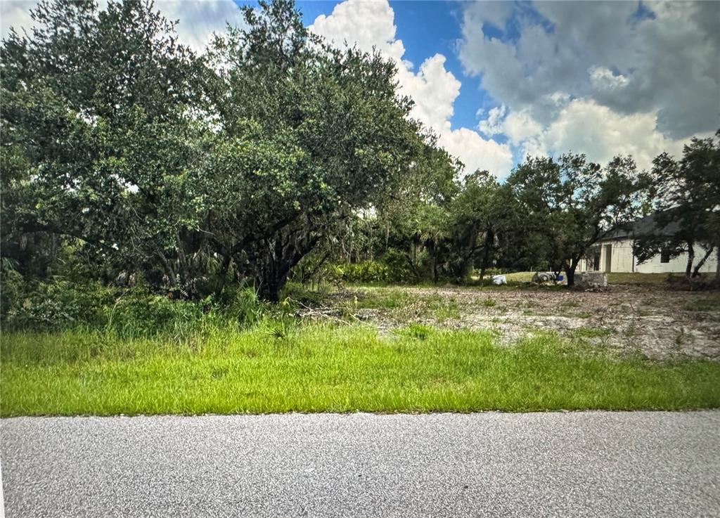 A vacant, partially cleared lot features mature trees and grass along a paved road — 17504 BILLIAR AVENUE, PORT CHARLOTTE, FL