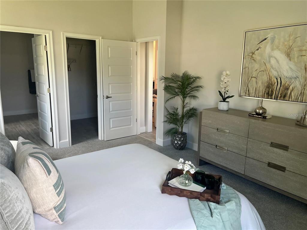 A bedroom features a bed, a dresser with artwork, and three open doorways — 12909 OGDEN GLADE RD STREET, DADE CITY, FL