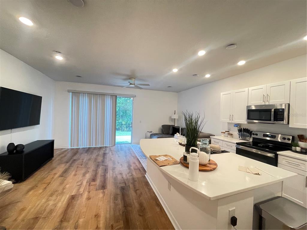An open-concept kitchen and living area features white cabinetry, a large island, and wood flooring — 3575 DAVENPORT CREEK COURT, KISSIMMEE, FL