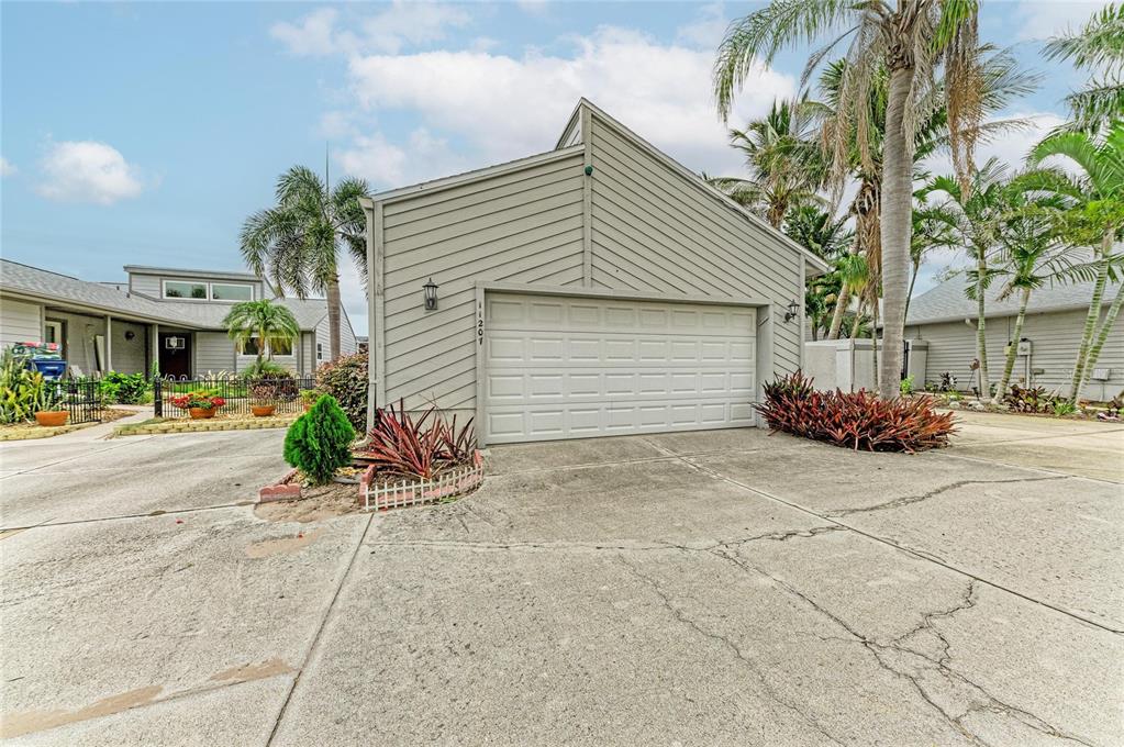 A beige house exterior features a two-car garage, a concrete driveway, and surrounding palm trees — 11207 LONGWOOD CT, BRADENTON, FL