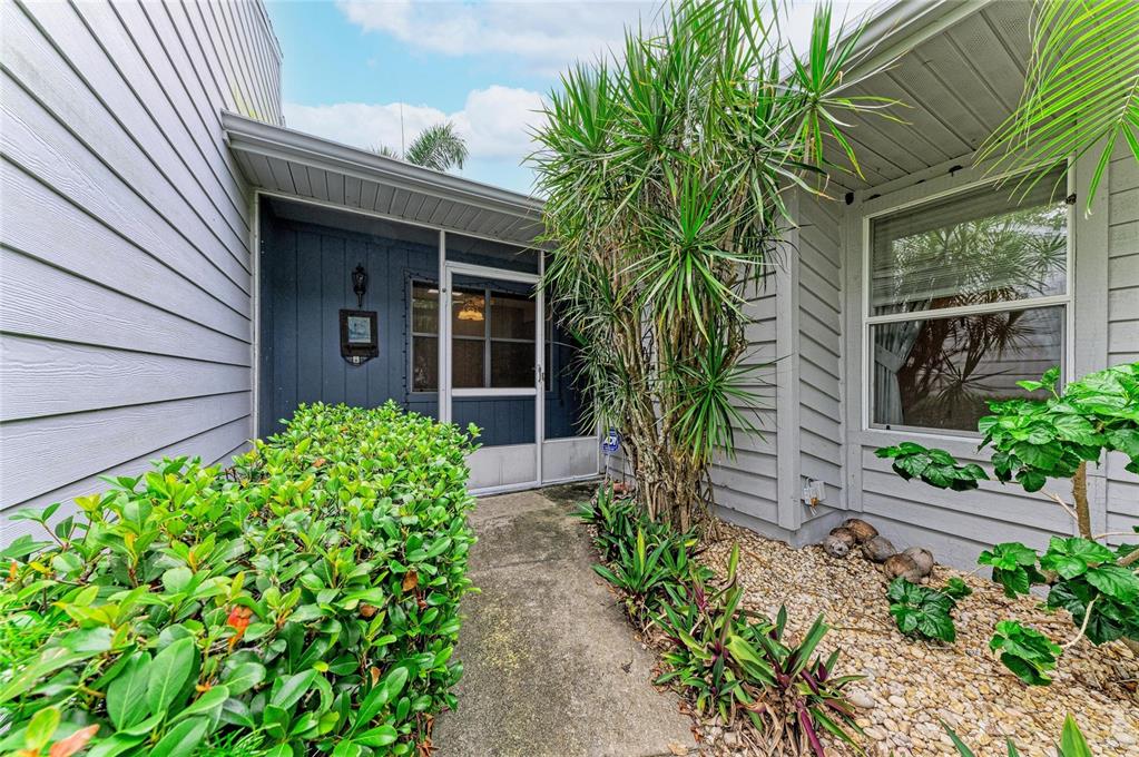 A concrete walkway leads to a screened front entryway of a house with gray siding — 11207 LONGWOOD CT, BRADENTON, FL