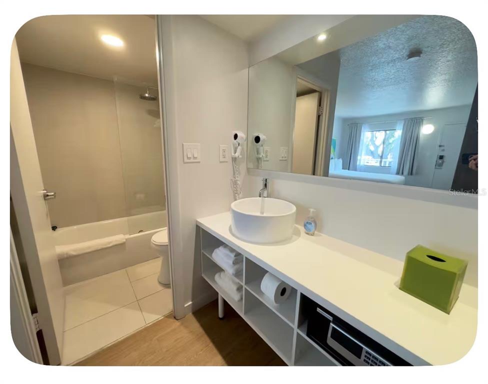 A bathroom with a vessel sink, open shelving, and an adjacent tub and shower area — 5367 W IRLO BRONSON MEMORIAL HIGHWAY UNIT 1-206, KISSIMMEE, FL