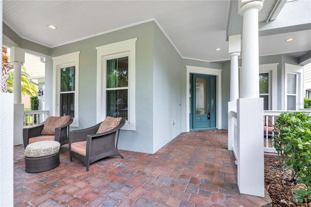 A covered front porch features brick pavers, two wicker chairs, and a teal front door — 11734 ALDENDALE STREET, ORLANDO, FL