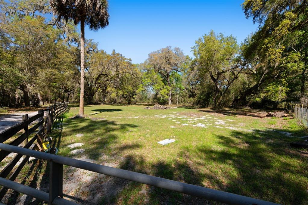 A grassy, fenced-in yard features mature trees and a palm tree under a clear sky — 15311 SW 107TH STREET, ARCHER, FL