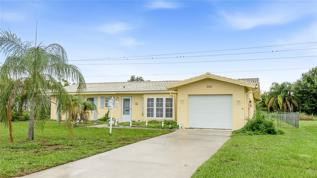A single-story house with a yellow exterior, a white garage door, and a palm tree — 113 ANNAPOLIS LANE, ROTONDA WEST, FL