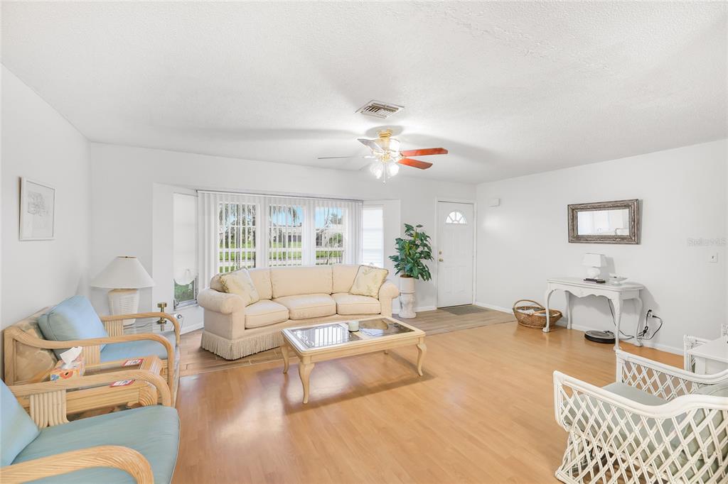 A living room features light wood flooring, a beige sofa, wicker chairs, and a ceiling fan — 113 ANNAPOLIS LANE, ROTONDA WEST, FL