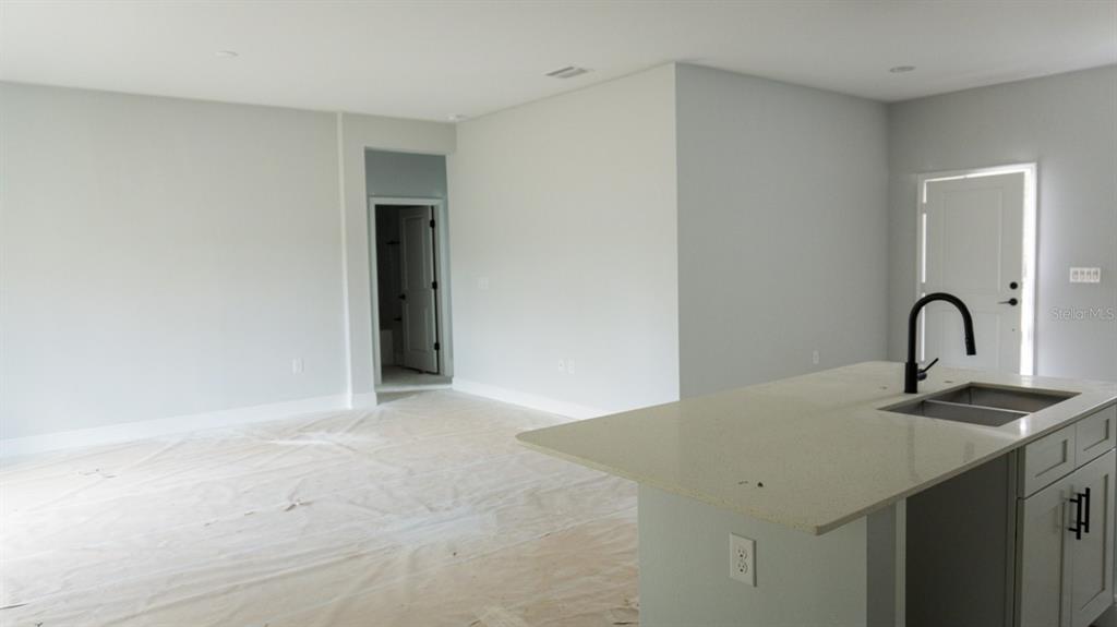 A kitchen island with a sink and faucet overlooks an empty room with light walls — 105 PONOKA STREET, PORT CHARLOTTE, FL