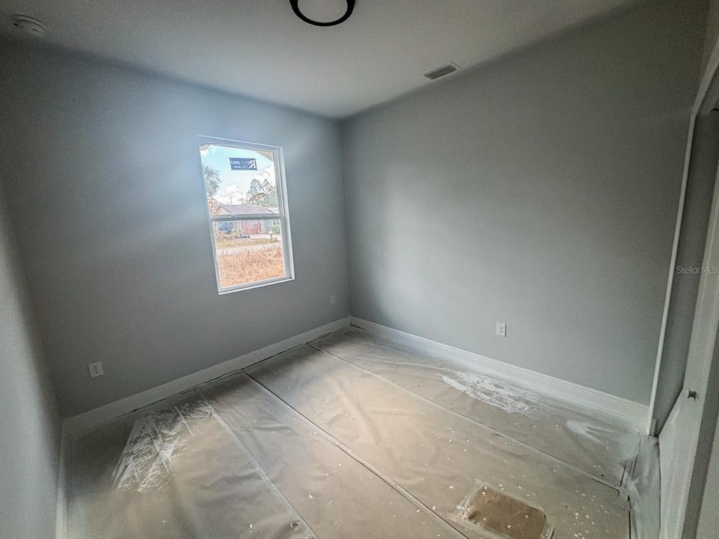 An empty bedroom features light gray walls, white trim, and a floor covered in plastic — 105 PONOKA STREET, PORT CHARLOTTE, FL