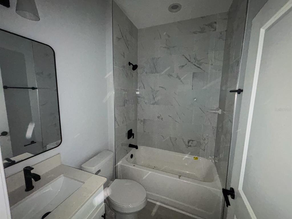 A bathroom features a white vanity, a toilet, and a bathtub with marble-look tile walls — 105 PONOKA STREET, PORT CHARLOTTE, FL
