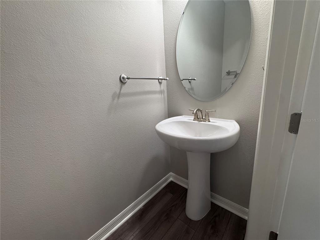 A half bathroom features a white pedestal sink, an oval mirror, and dark wood flooring — 2518 CAGLIARI LANE, APOPKA, FL
