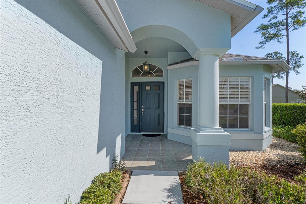 The exterior of a light blue house features a covered entryway with a white column — 18236 WEBSTER GROVE DRIVE, HUDSON, FL