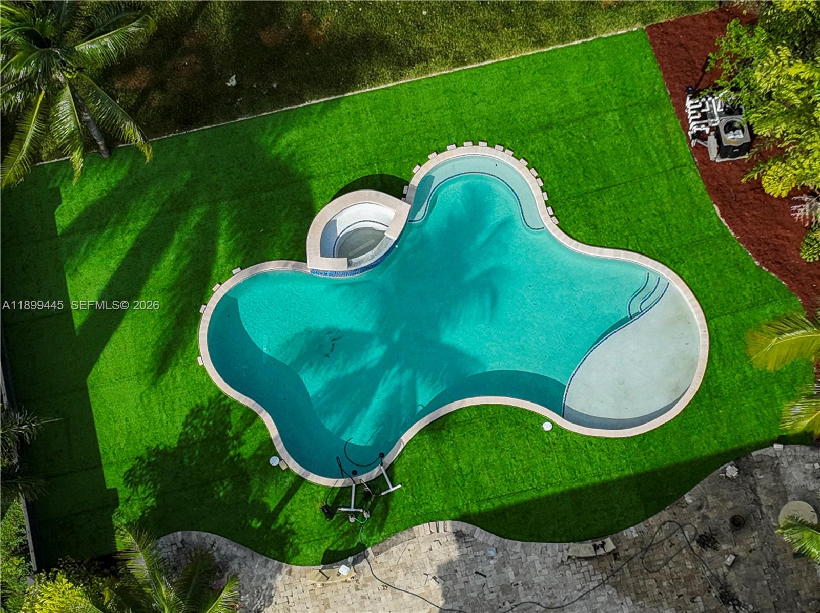 An aerial view shows a freeform swimming pool with an attached spa surrounded by artificial turf — 112 NW 14th Way, Dania Beach FL 33004, DANIA BEACH, FL