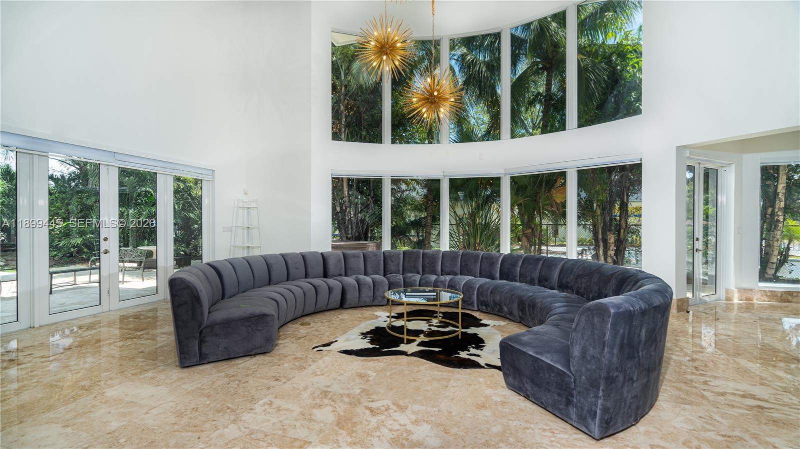 A spacious living room features a large curved sofa, floor-to-ceiling windows, and tile flooring — 112 NW 14th Way, Dania Beach FL 33004, DANIA BEACH, FL