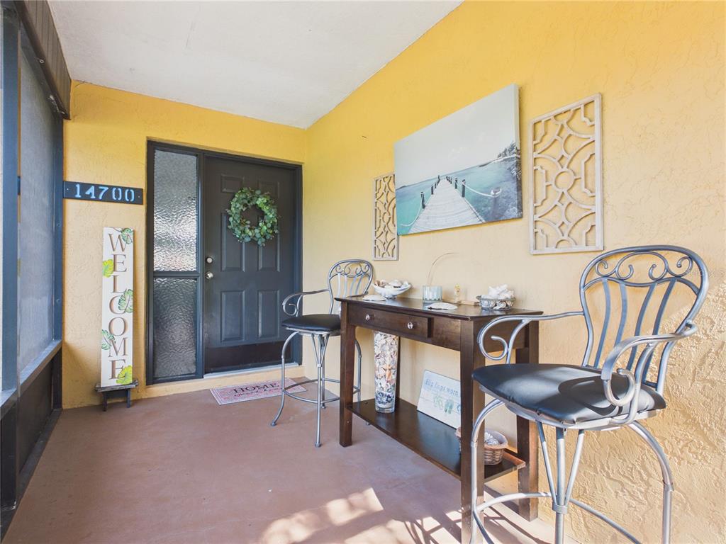 A covered porch features yellow walls, a dark front door, two metal chairs, and a table — 14700 SE 94TH AVENUE, SUMMERFIELD, FL