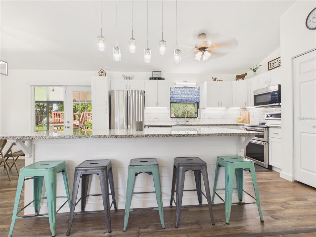 A kitchen features a large granite-topped island with five metal stools and white cabinetry — 14700 SE 94TH AVENUE, SUMMERFIELD, FL