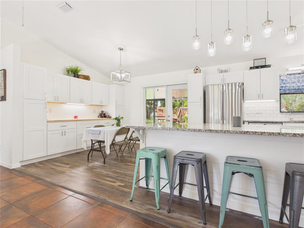 A kitchen features white cabinetry, a granite-topped island with metal stools, and wood-look flooring — 14700 SE 94TH AVENUE, SUMMERFIELD, FL