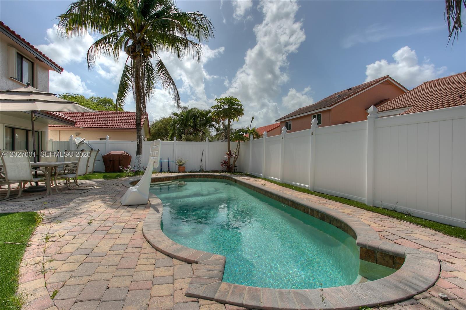 A backyard features a swimming pool, brick paver patio, palm tree, and white vinyl fence — 9521 NW 18th Mnr, Plantation FL 33322, PLANTATION, FL