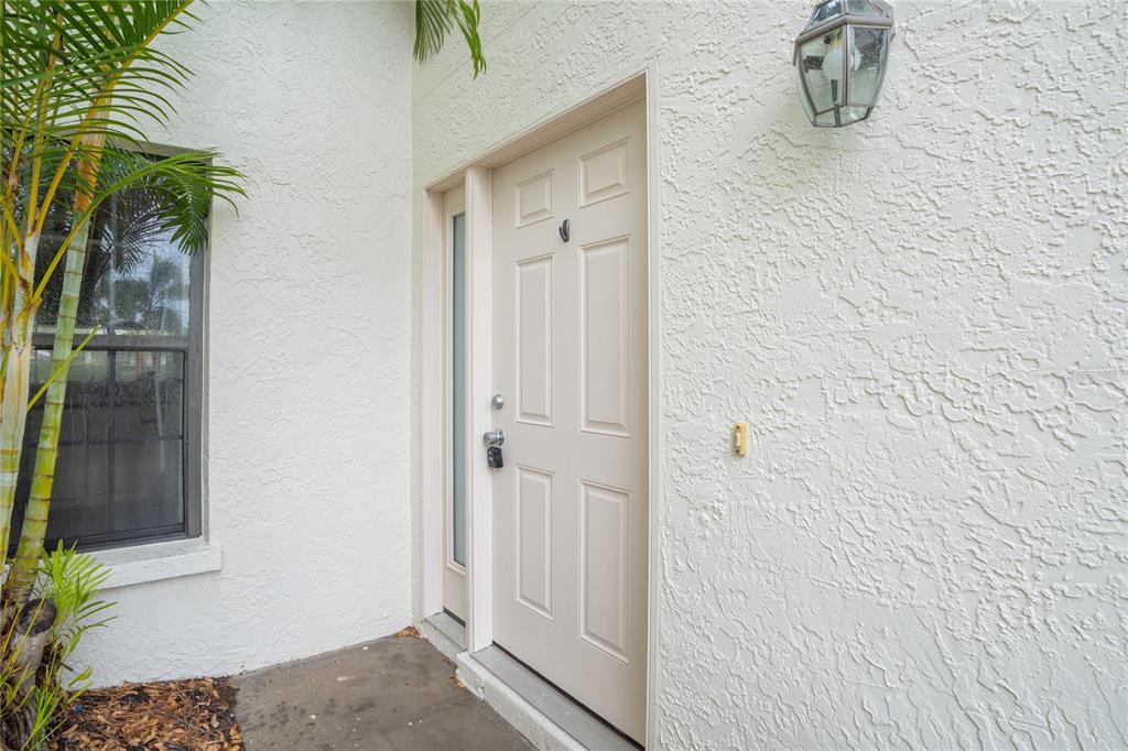 A white front door with a side window is set in a textured stucco wall — 4717 WINSLOW BEACON UNIT 7, SARASOTA, FL