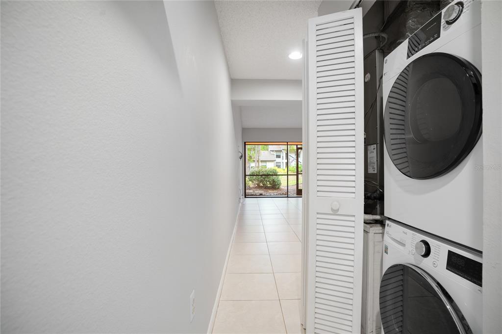 A laundry closet with a stacked washer and dryer sits beside a tiled hallway — 4717 WINSLOW BEACON UNIT 7, SARASOTA, FL