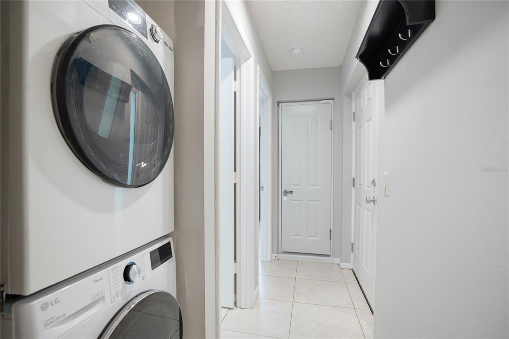 A laundry area with a stacked LG washer and dryer next to a hallway with tiled floors — 4717 WINSLOW BEACON UNIT 7, SARASOTA, FL