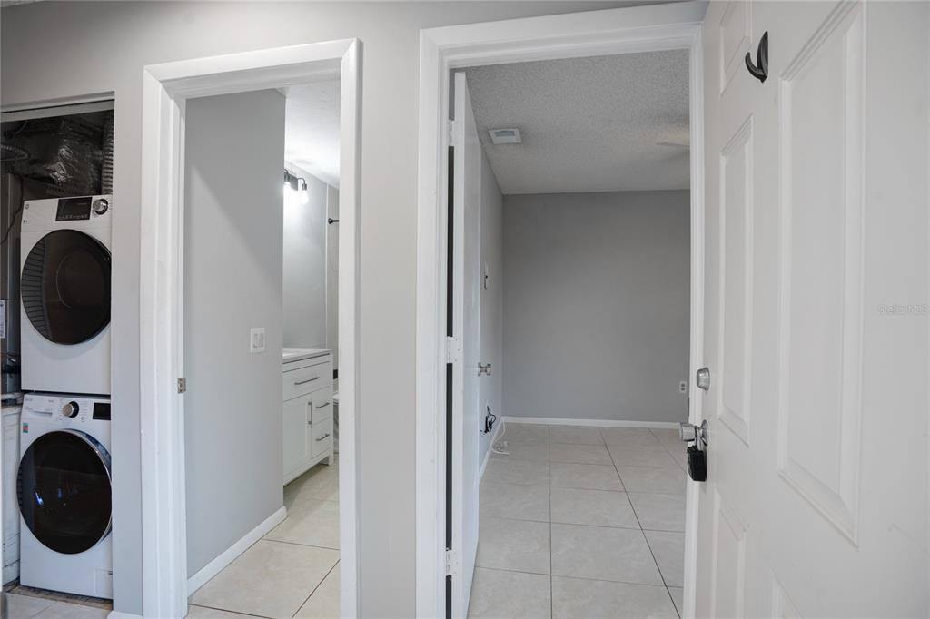 A laundry area with a stacked washer and dryer sits beside a bathroom and bedroom — 4717 WINSLOW BEACON UNIT 7, SARASOTA, FL