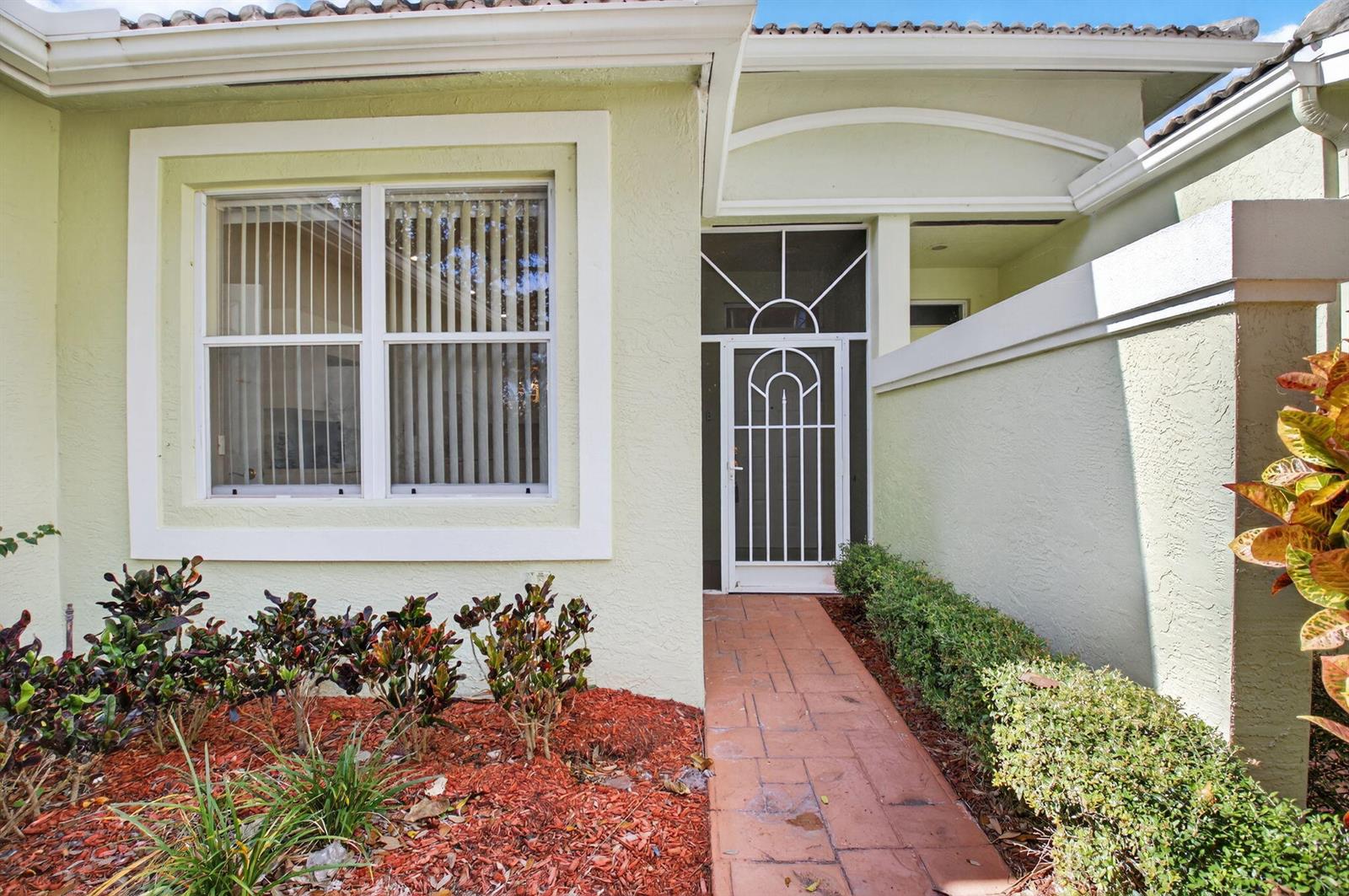 A pale green house exterior features a white screen door, a window, and a walkway — 10612 Royal Caribbean Circle, Boynton Beach FL 33437, BOYNTON BEACH, FL