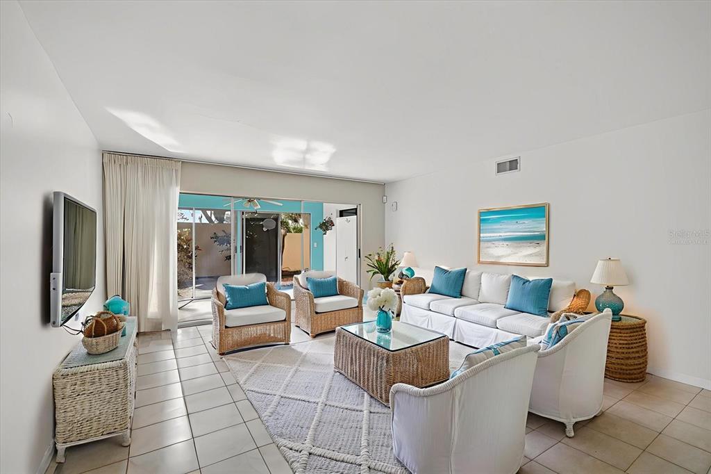 A bright living room features white tile floors, wicker furniture, and sliding glass patio doors — 1111 W FAITH CIRCLE UNIT 1003, BRADENTON, FL